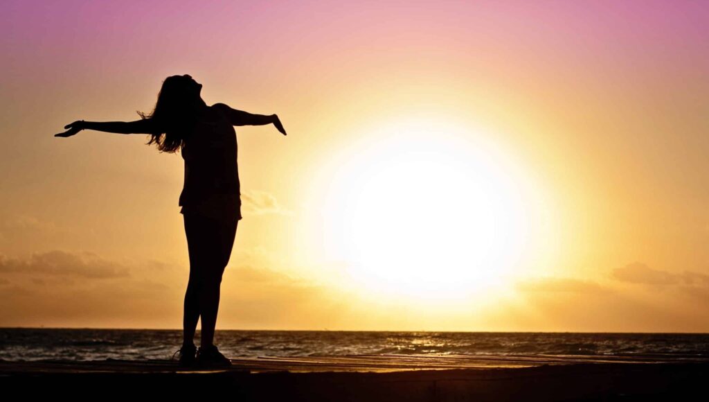 woman standing at beach during sunset celebrating recovery from drug addiction