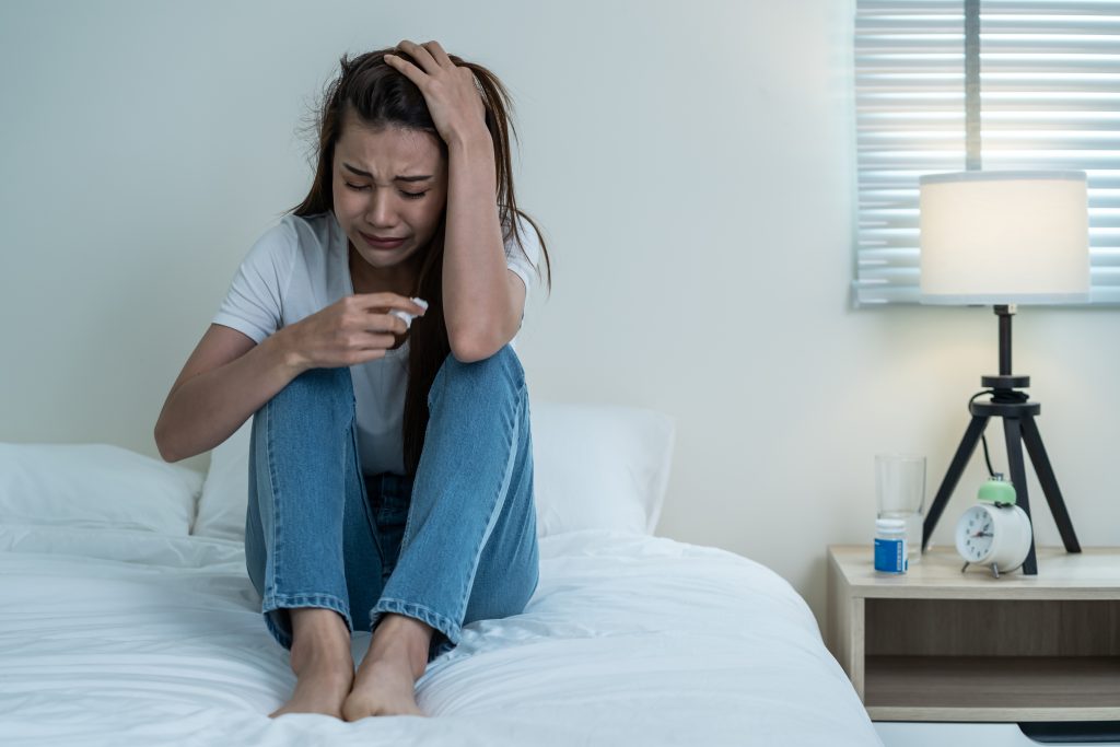 upset woman sitting on bed dealing with drug addiction