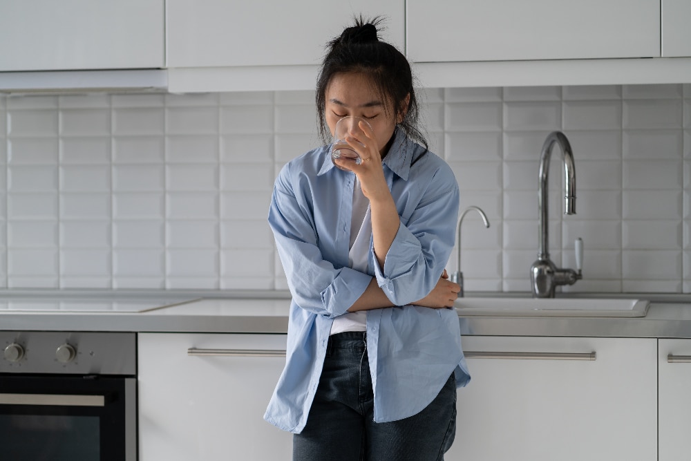 stressed woman standing art kitchen counter drinking water while going through a drug detox for opioids